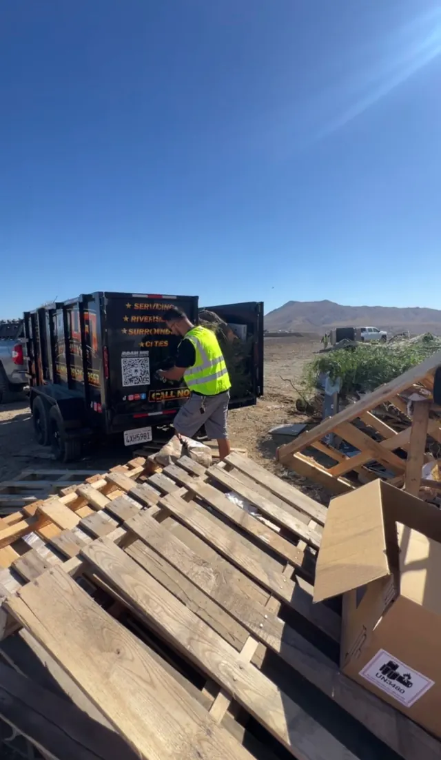 Crew member in a safety vest unloading wooden pallets beside the trailer